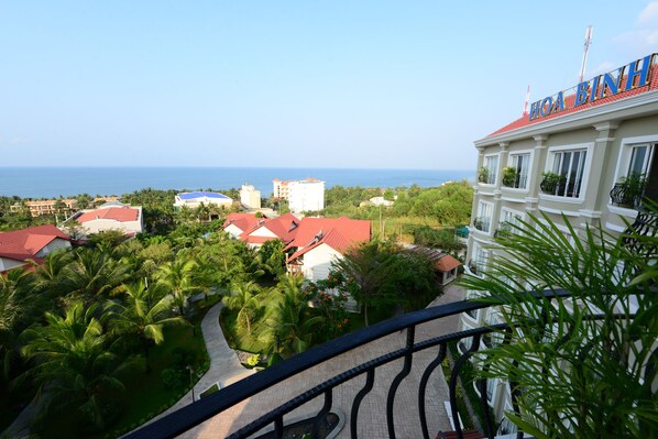 A hotel with a red roof, surrounded by lush greenery and a view of the sea.