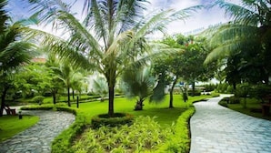 A landscaped garden with palm trees, a stone pathway, and neatly trimmed hedges. - Hoa Binh Phu Quoc Hotel (Phu Quoc)