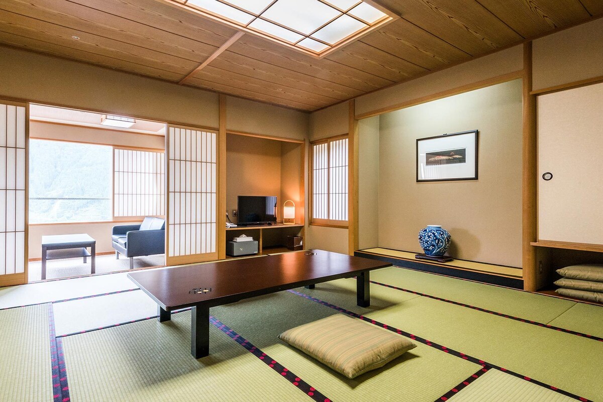 A tatami mat room with a low table, a television, a vase, and a sofa.