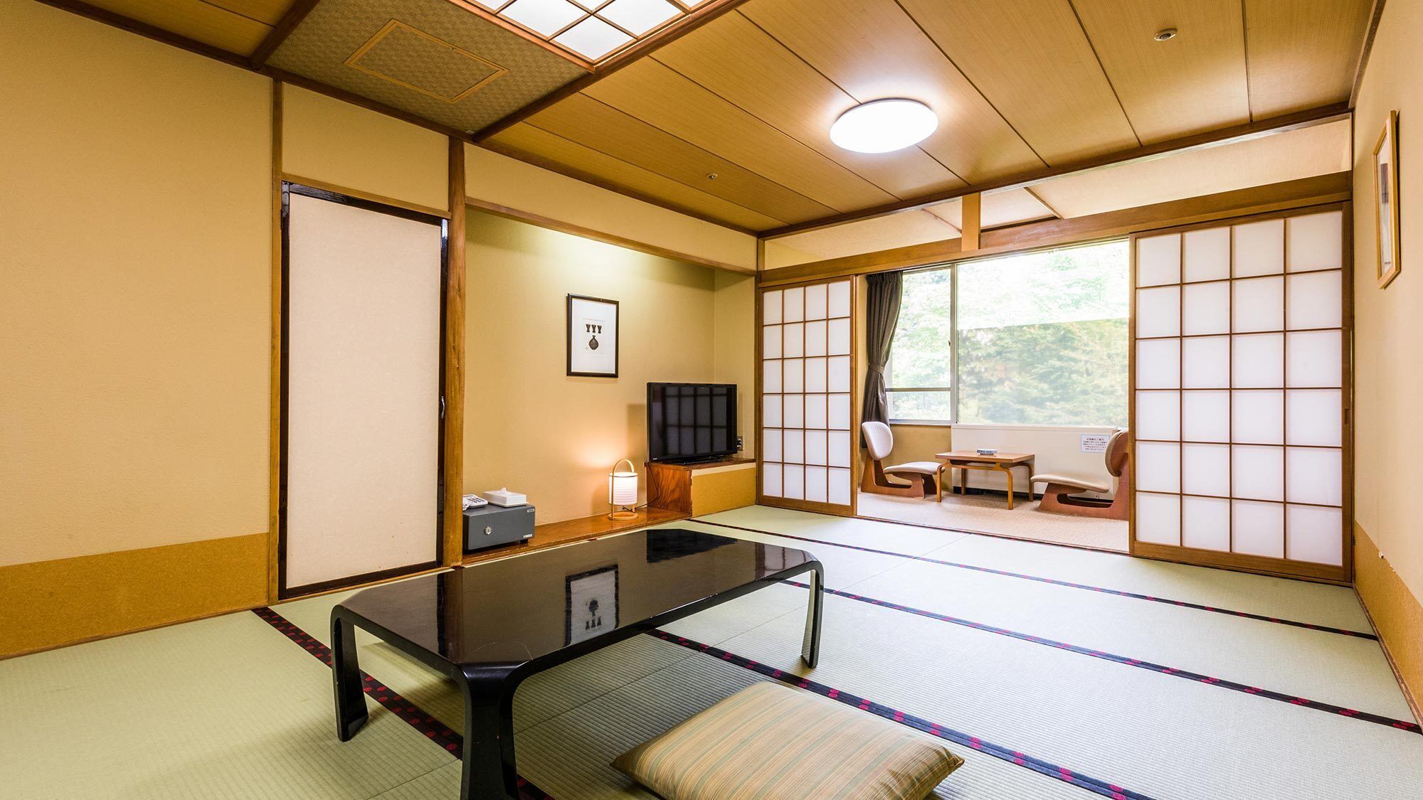 Une pièce de style japonais traditionnel, avec un sol recouvert de tatamis, une table basse, un téléviseur et des portes coulissantes.