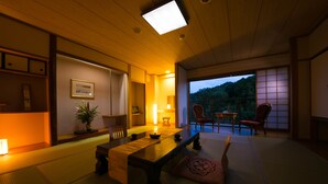 Una habitación japonesa tradicional con suelo de tatami, una mesa baja y puertas correderas que dan a un balcón con vistas a las montañas.