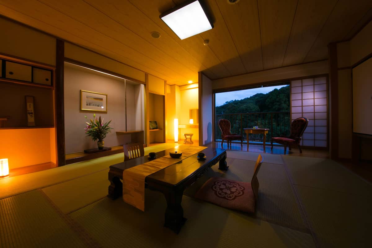 A traditional Japanese room with tatami flooring, a low table, and sliding doors leading to a balcony with a view of the mountains.