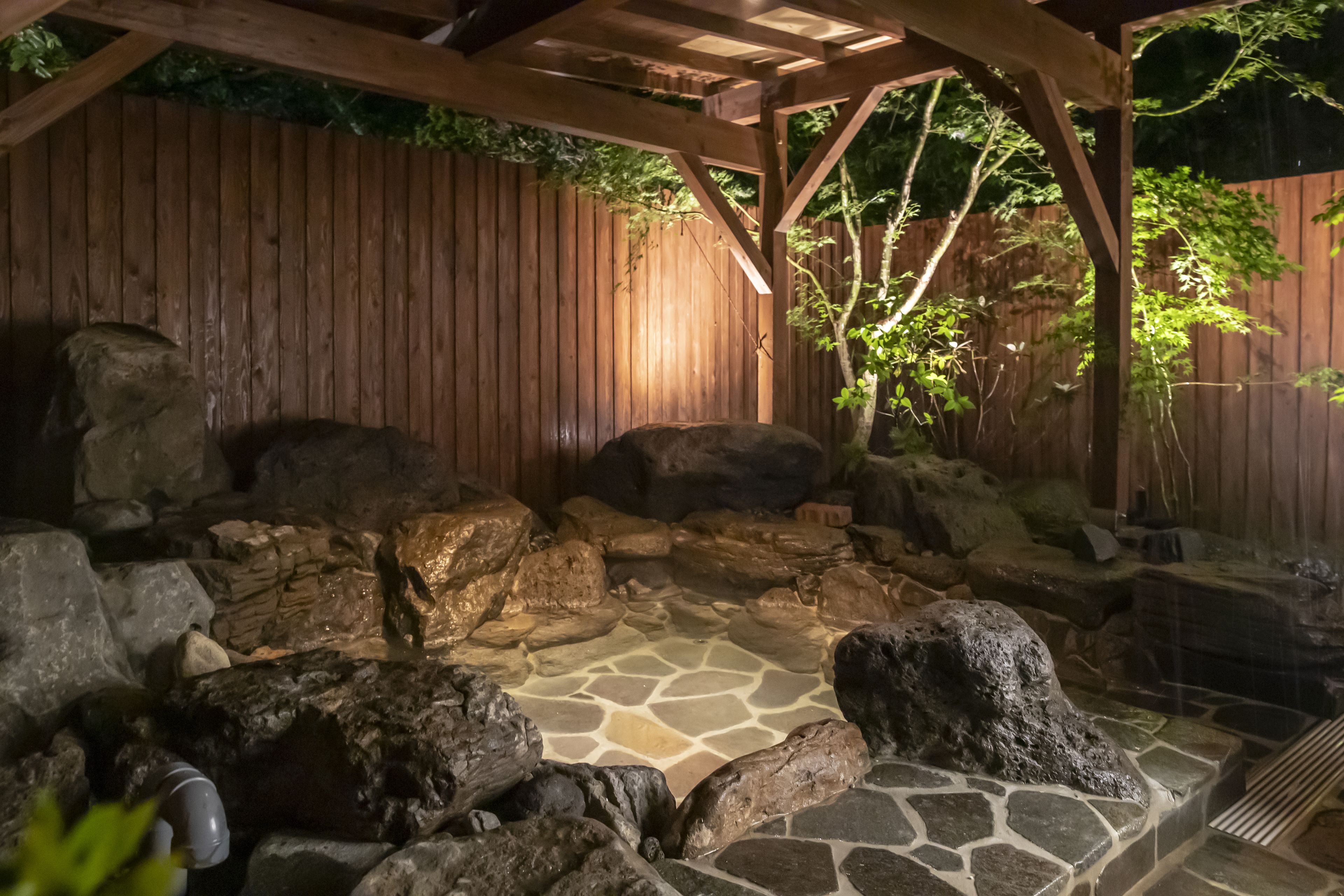 A stone hot tub surrounded by rocks and wooden structures.