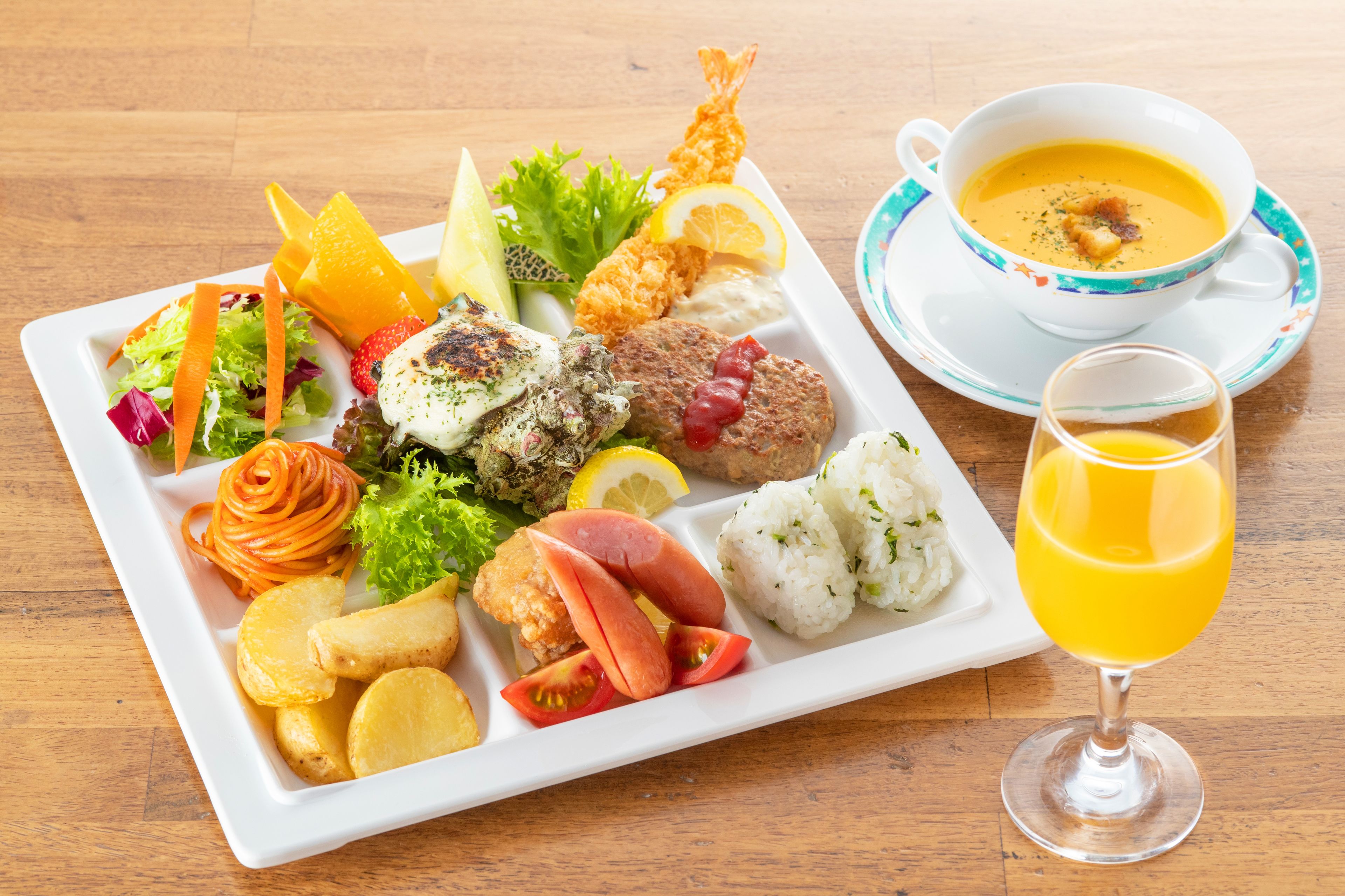 Ein weißer Teller mit verschiedenen Speisen, darunter Fisch, Gemüse und ein Glas Orangensaft.