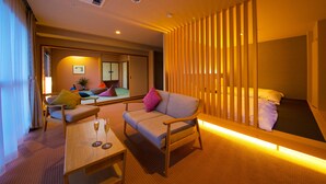 Habitación de hotel con sofá, una mesita con vasos, cama con almohadas, puerta corredera y vistas al exterior.
