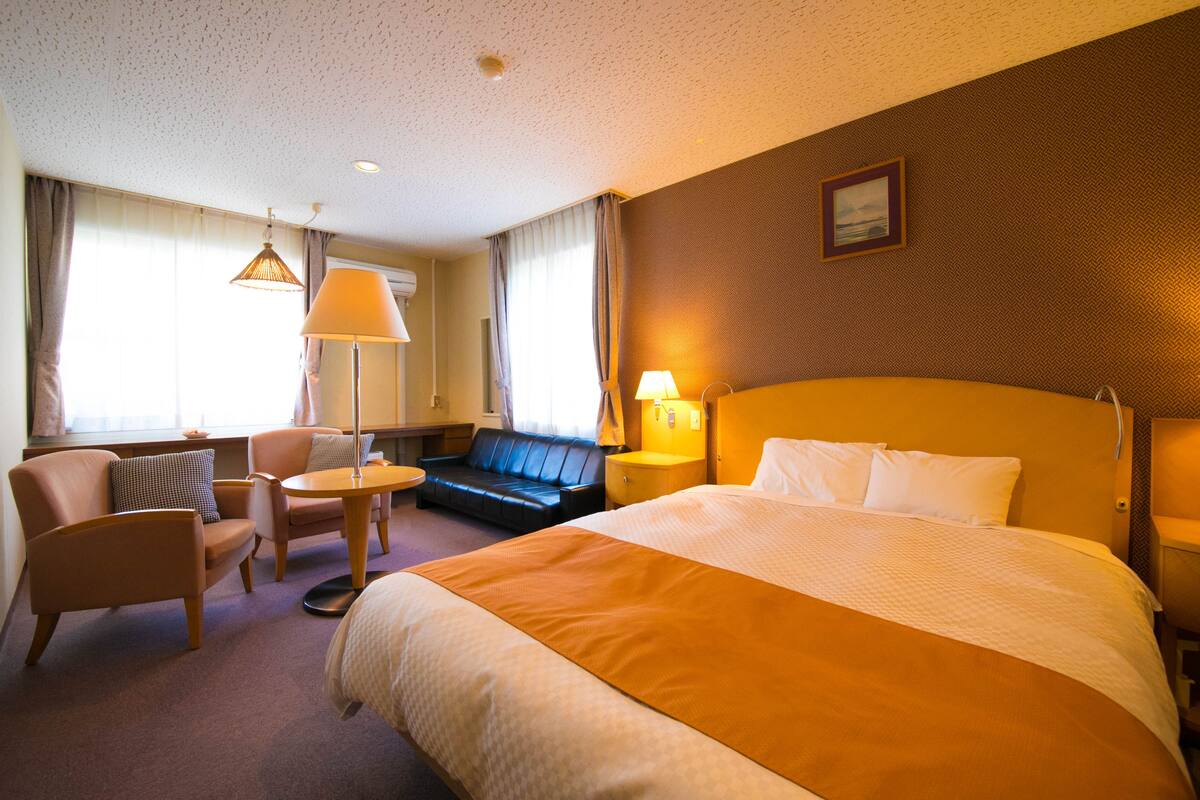 A hotel room with a large bed, a sofa, a small table, and a lamp.