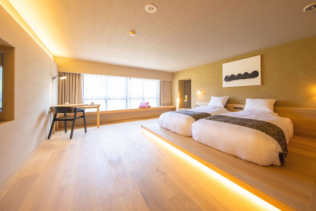 A modern hotel room with a large bed, a desk, and a window with curtains.
