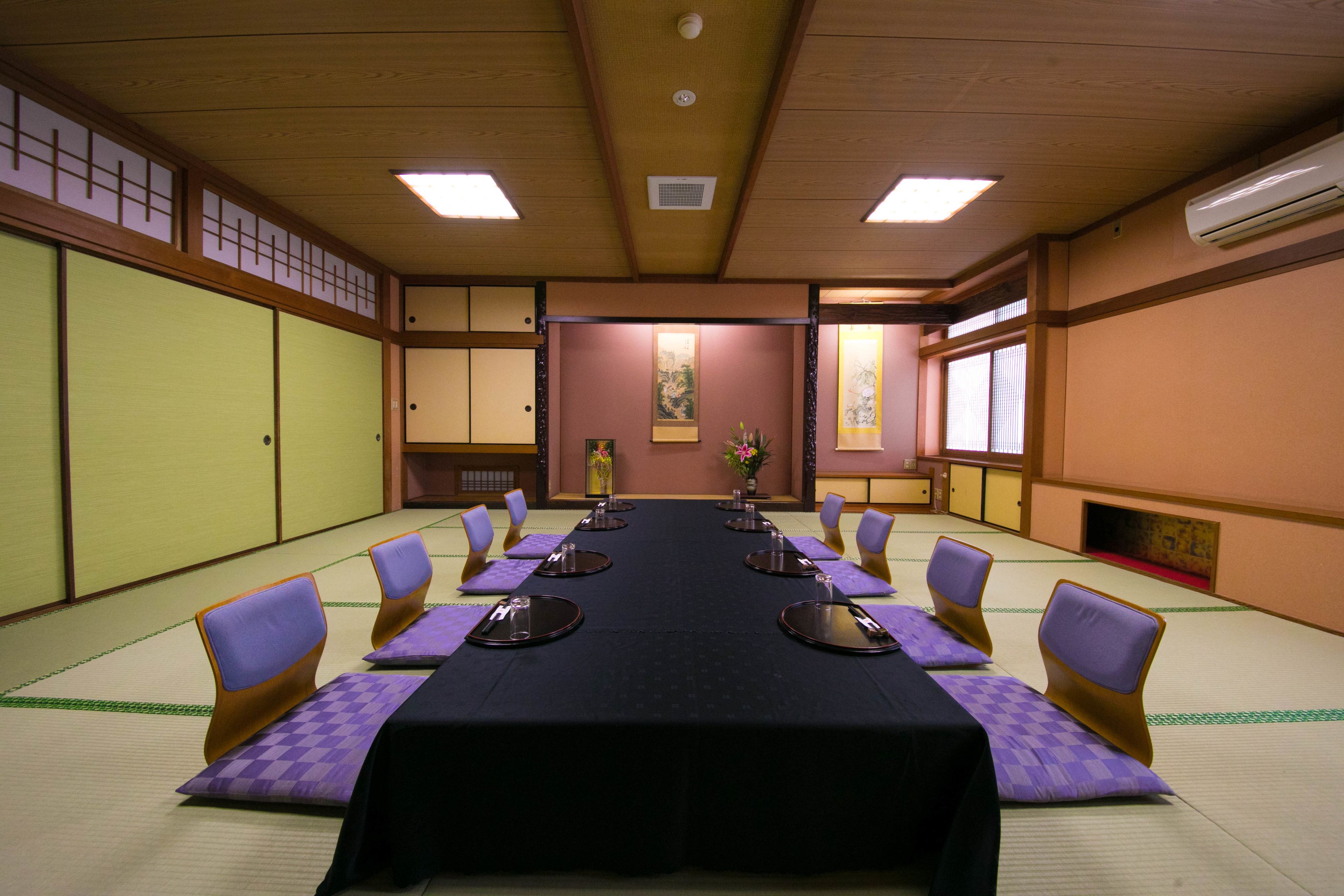 A traditional Japanese meeting room with tatami mats, a long table with round tables, and purple cushions.