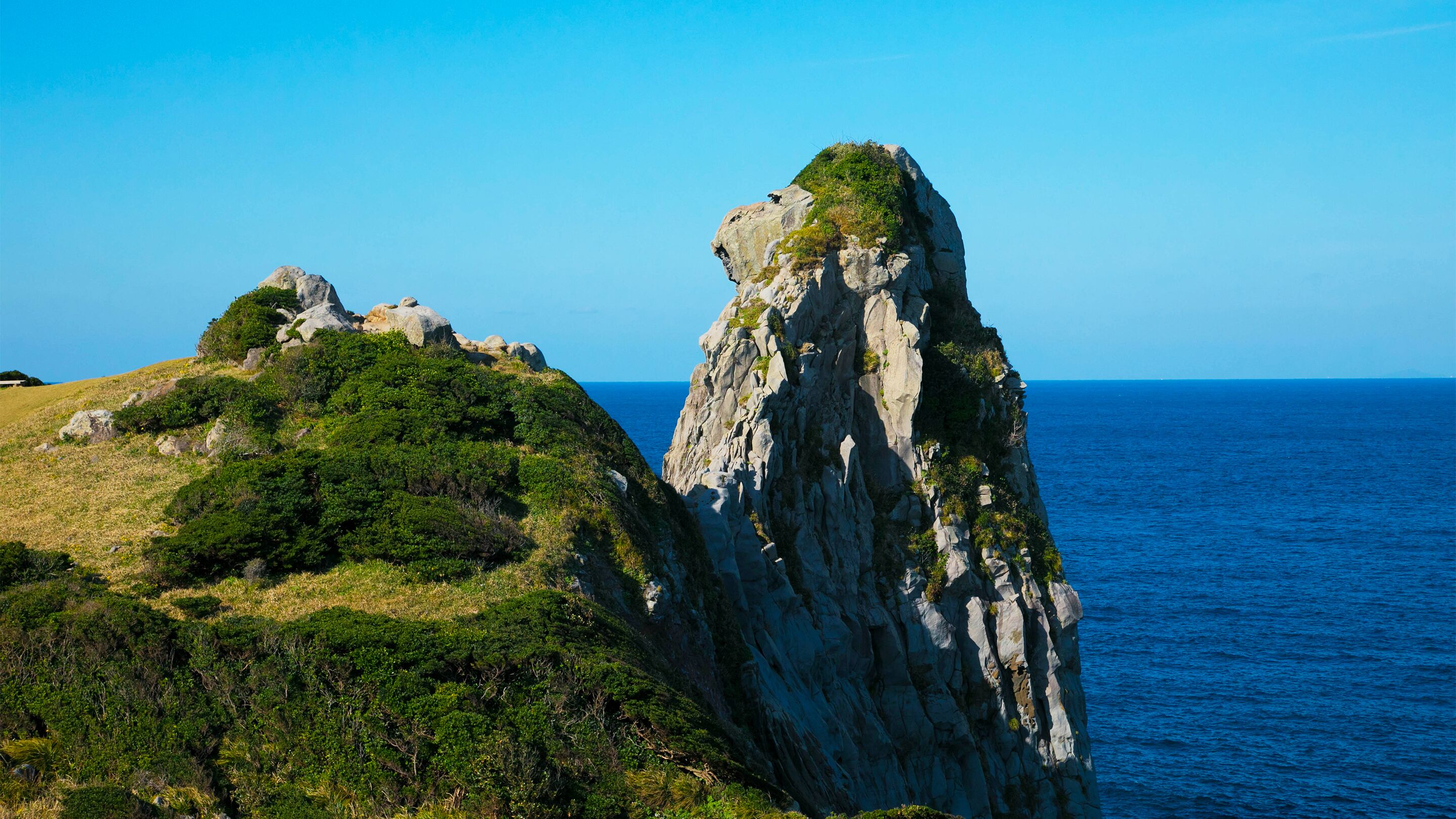 A coastal landscape with rocky cliffs and a clear view of the sea.