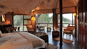 A spacious room with a large bed, a desk, and two chairs. There is a window providing a view of the outdoors. - Hamiltons Tented Camp (KRUGER NATIONAL PARK)