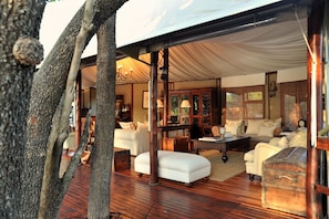 A cozy, well-lit room with a wooden floor, a sofa, a table, and a lamp. - Hamiltons Tented Camp (KRUGER NATIONAL PARK)