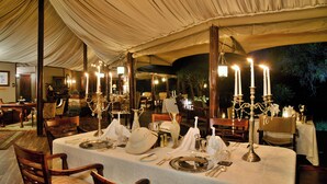 A tented dining area with tables set for a meal, candle-lit chandeliers, and a view of the night sky. - Hamiltons Tented Camp (KRUGER NATIONAL PARK)