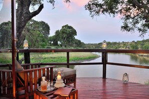 A wooden deck with a table set for dining, overlooking a body of water and trees. - Hamiltons Tented Camp (KRUGER NATIONAL PARK)