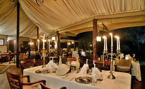 A tented dining area with tables set for a meal, candle-lit chandeliers, and a view of the night sky. - Hamiltons Tented Camp (KRUGER NATIONAL PARK)