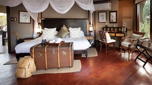 A bedroom with a large bed, a desk, and a chair. There are suitcases and a backpack on the floor. - Hamiltons Tented Camp (KRUGER NATIONAL PARK)