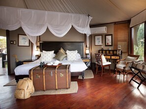 A bedroom with a large bed, a desk, and a chair. There are suitcases and a backpack on the floor. - Hamiltons Tented Camp (KRUGER NATIONAL PARK)