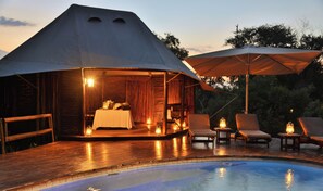 A tented accommodation with a pool, wooden deck, and outdoor seating.