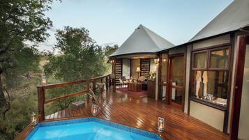 A wooden deck with a swimming pool, a lounge area with a sofa and table, and a large window.