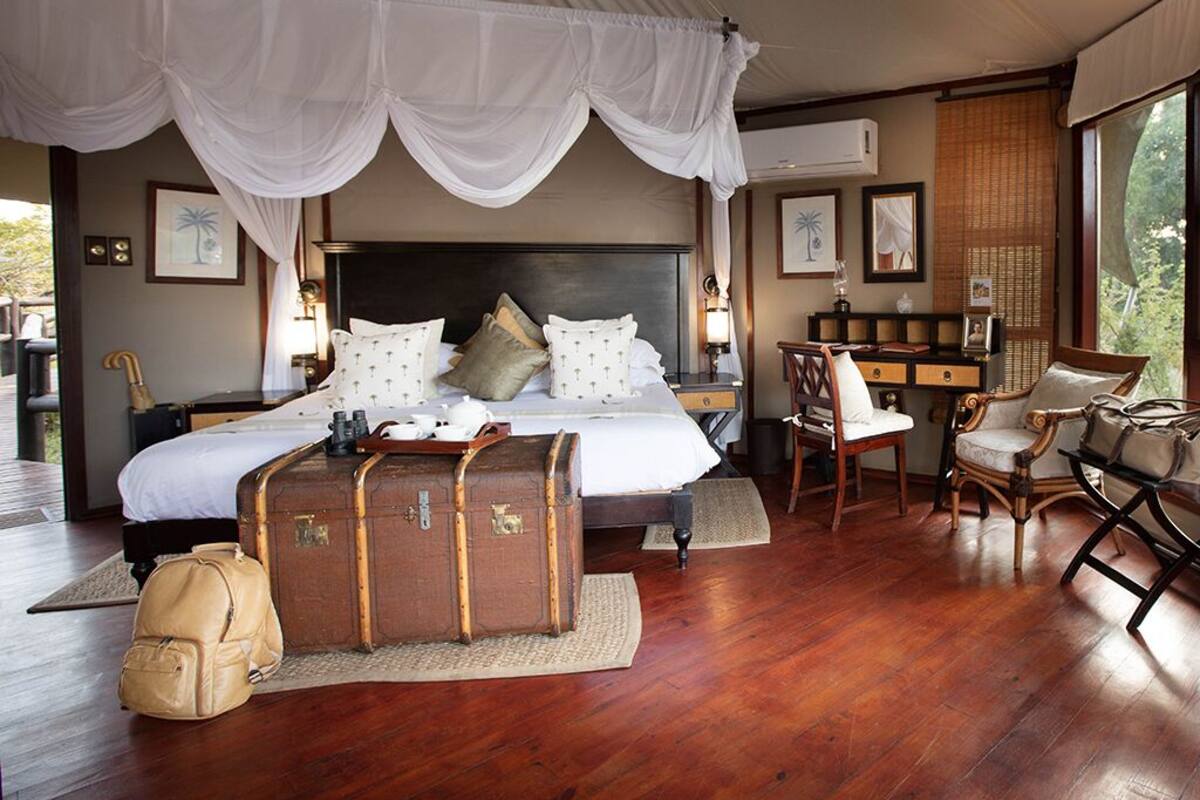 A bedroom with a large bed, a desk, and a chair. There are suitcases and a backpack on the floor.