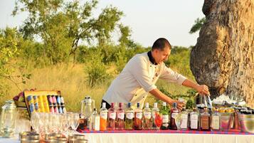 A person pouring a drink from a bottle into a glass on a table with various bottles and cans.