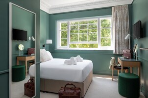 A neatly arranged hotel room with a large bed, a desk, a chair, a TV, and a window with a view of trees.