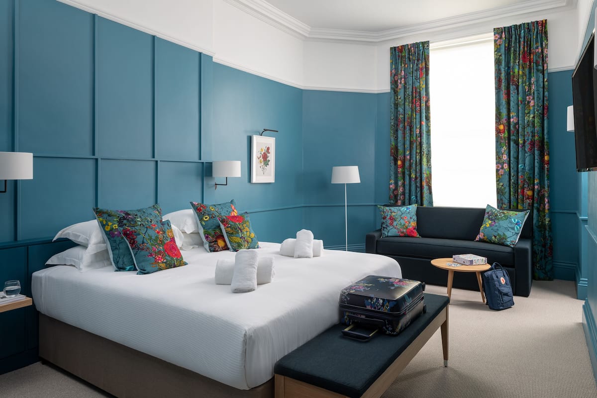 Ein modernes Hotelzimmer mit einem großen Bett, einer Sitzecke, einem kleinen Tisch und einer Bank.