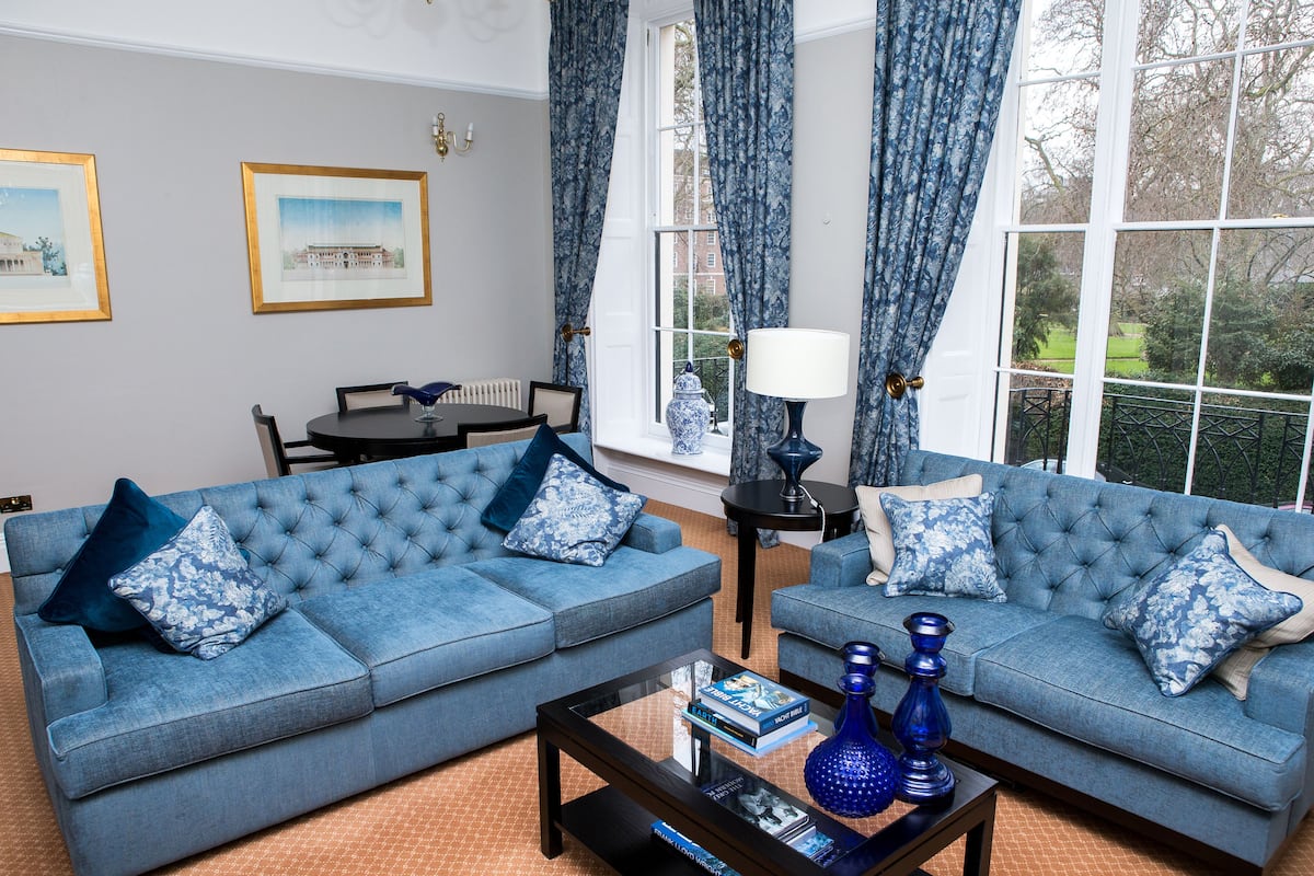 Ein Wohnzimmer mit zwei blauen Sofas, einem Couchtisch und Blick auf einen Garten durch große Fenster.