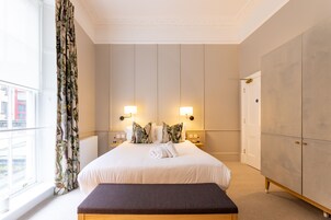 A hotel room with a large bed, two bedside lamps, a wardrobe, and a view of the city.