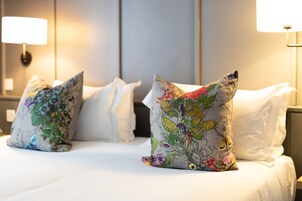 Ein Hotelzimmer mit einem ordentlich bezogenen Bett, Kissen mit Blumenmuster und zwei Nachttischlampen.
