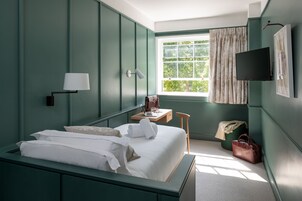 Une chambre d’hôtel avec un lit, un bureau avec un ordinateur portable, une chaise, une télévision et une fenêtre avec des rideaux.