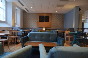 A modern restaurant with a central seating area featuring sofas and tables, a patterned wall, and a large TV screen.