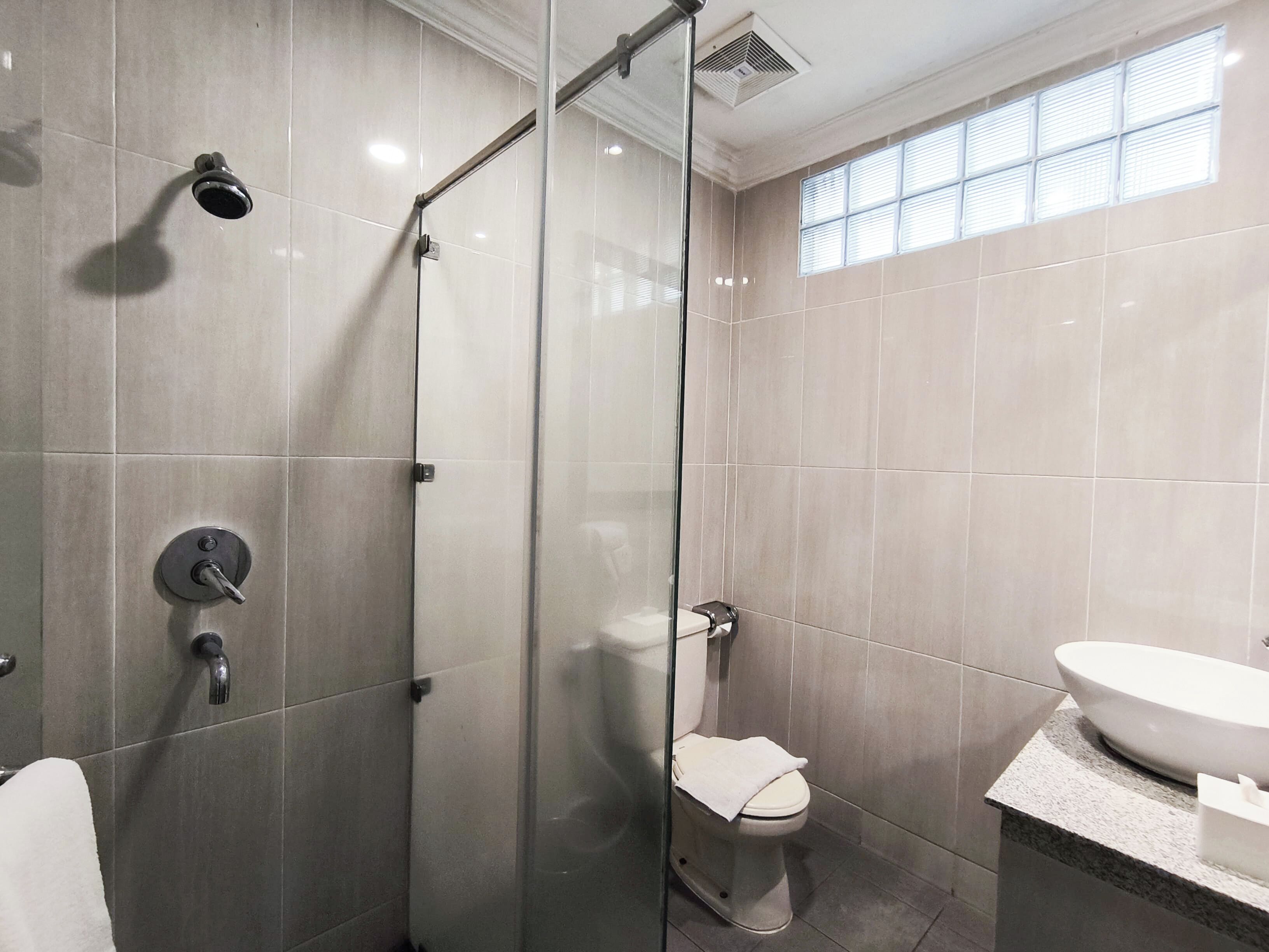 Un baño moderno con ducha de vidrio, inodoro y lavamanos con encimera de mármol.