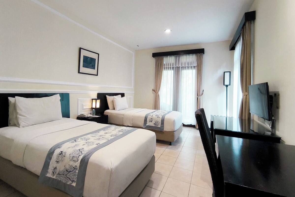 A hotel room with two beds, a desk, a television, and a window with curtains.