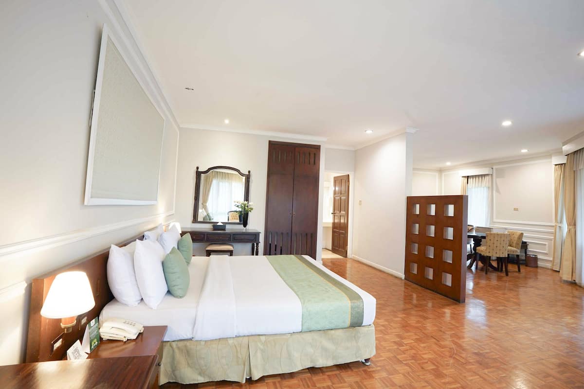 A hotel room with a bed, bedside table, lamp, dresser, mirror, and a partition wall.