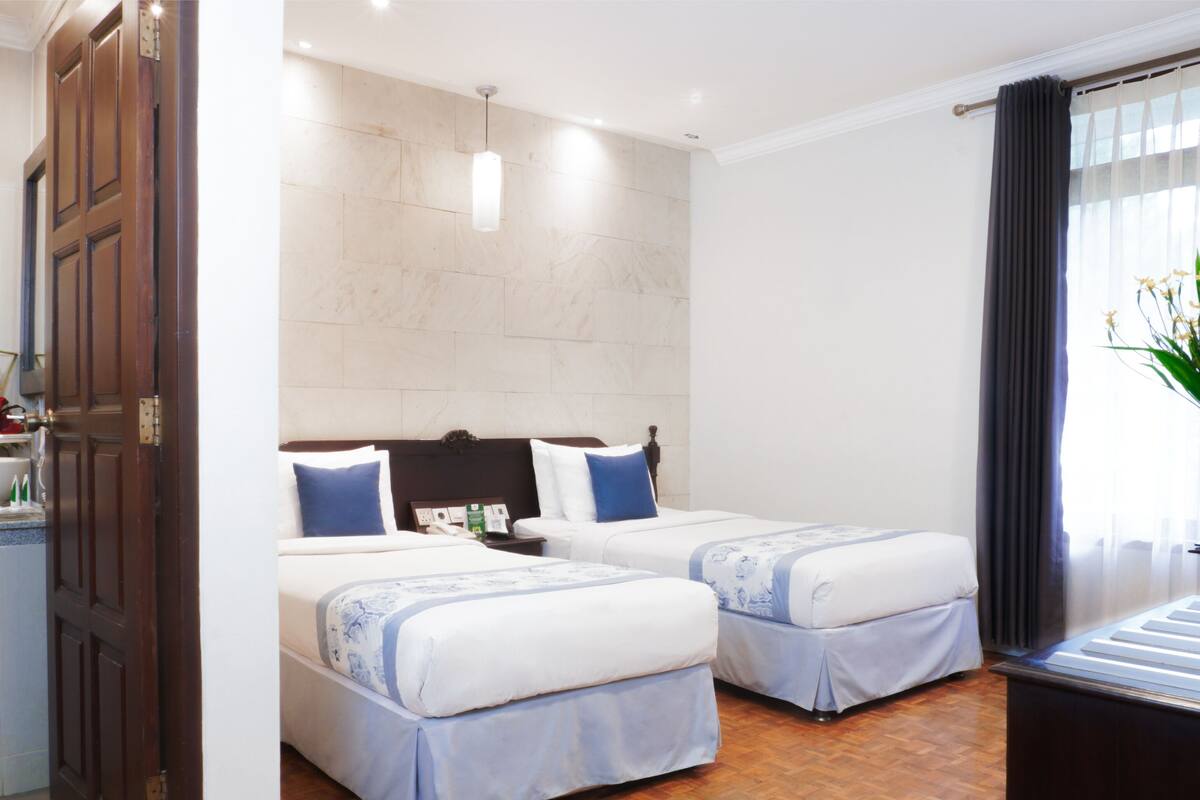 A hotel room with two beds, a bathroom with a sink and mirror, and a large window with curtains.