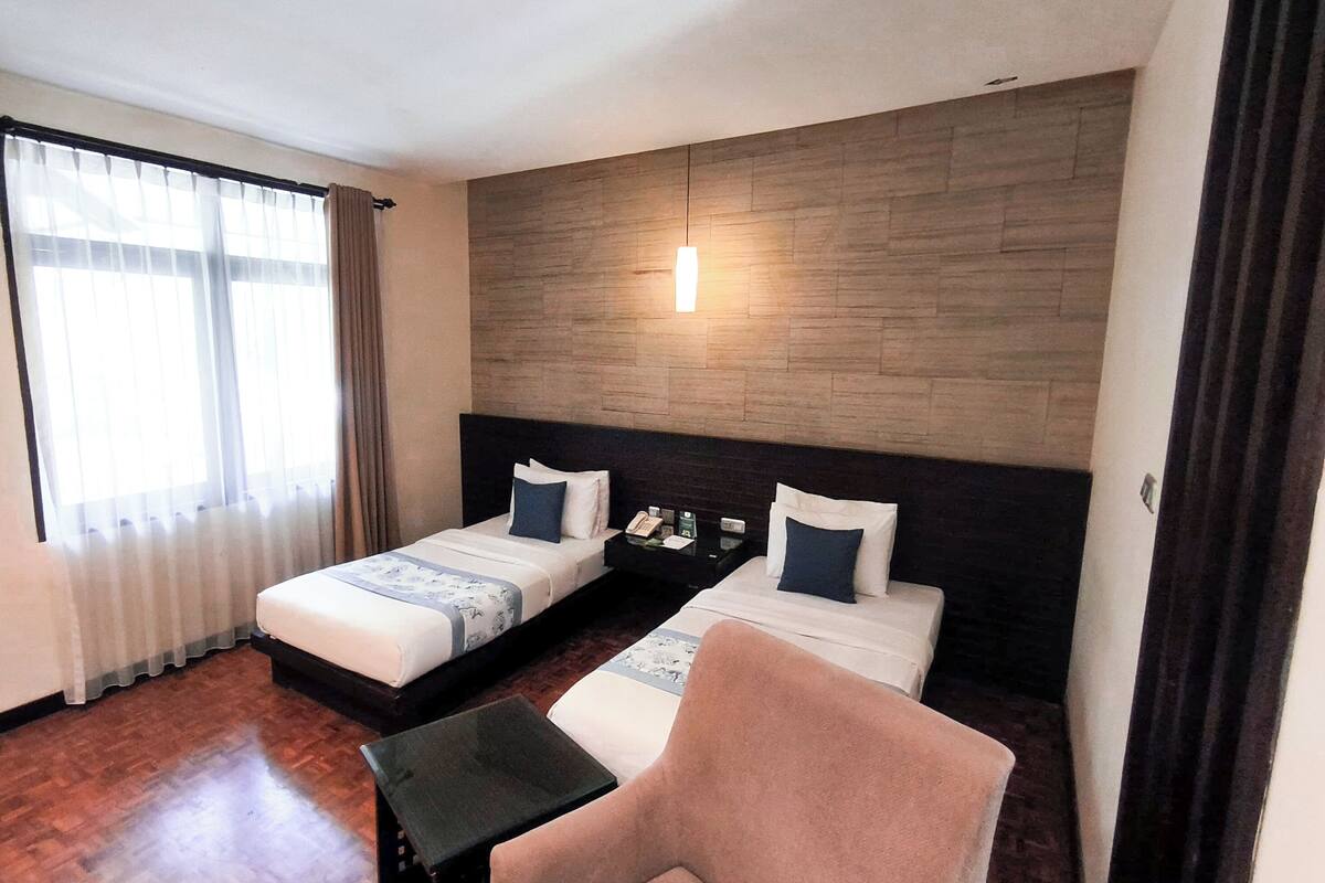 A hotel room with two beds, a small table, a chair, and a wooden accent wall.