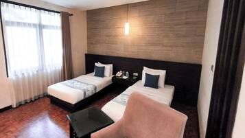 Habitación de hotel con dos camas, una mesita, una silla y una pared decorativa de madera.