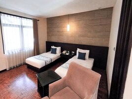 Habitación de hotel con dos camas, una mesita, una silla y una pared decorativa de madera.