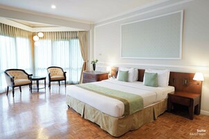 Una suite de hotel con una cama grande, dos sillones, una mesita y una mesita de noche con lámpara.