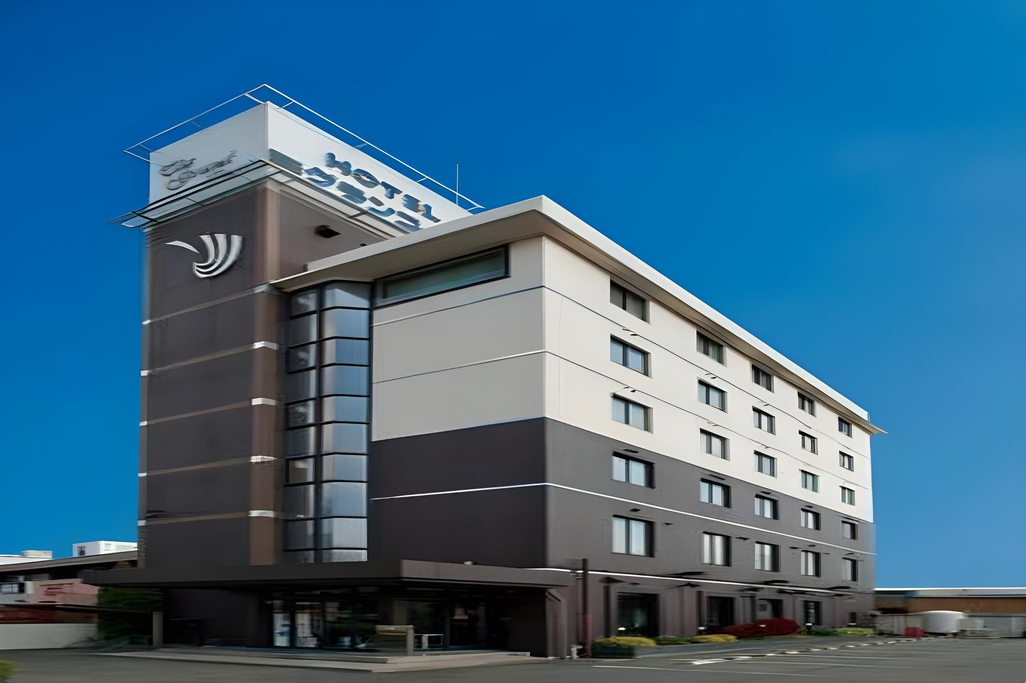 A multi-story hotel with a prominent sign on the corner, large windows, and a flat roof.