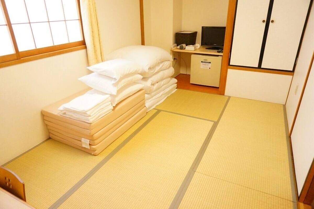 A room with tatami flooring, a bed with white bedding, a desk with a computer, and a wardrobe.