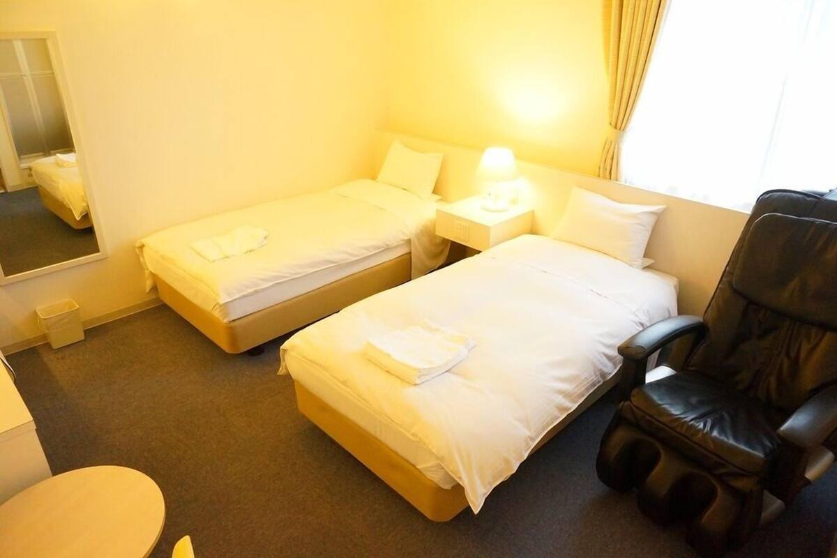 A hotel room with two beds, a massage chair, a small table, and a mirror.