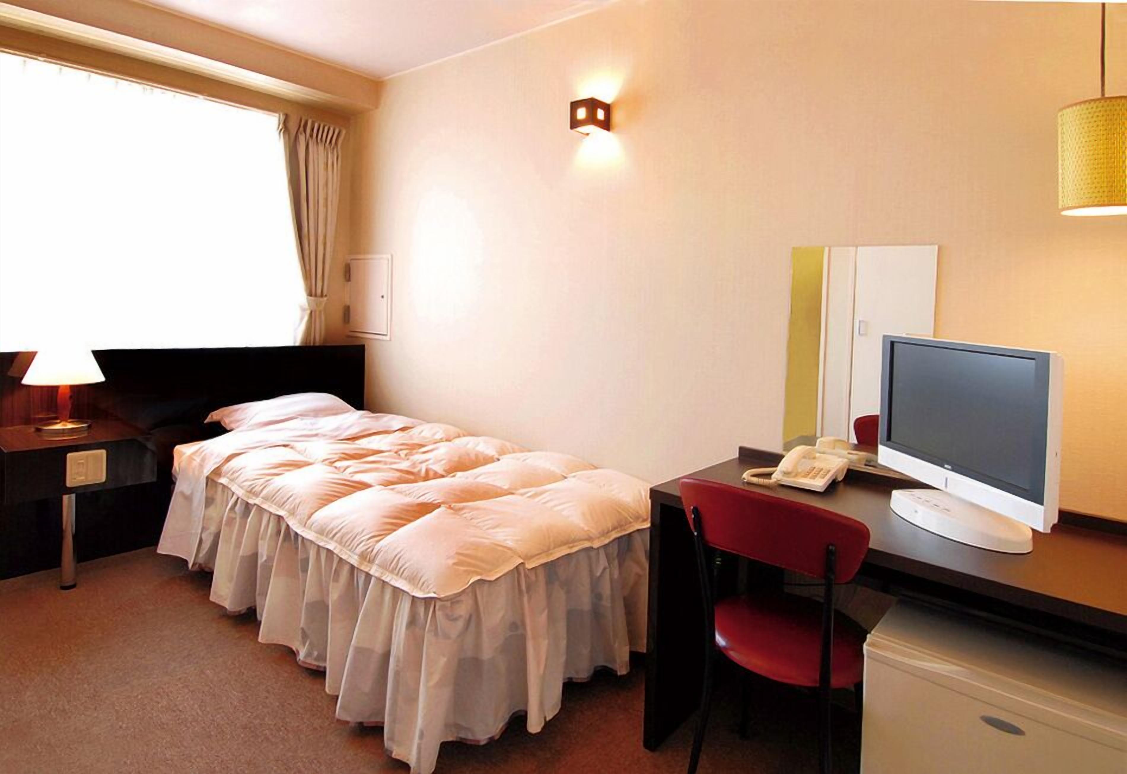 Une chambre d’hôtel équipée d’un lit, d’un bureau, d’une chaise, d’un ordinateur et d’une fenêtre avec des rideaux.
