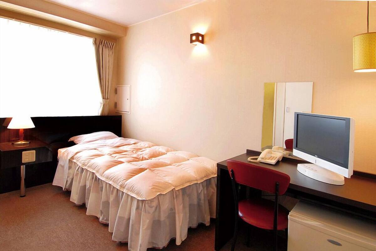 A hotel room with a bed, desk, chair, computer, and a window with curtains.