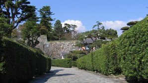 A stone pathway flanked by neatly trimmed hedges, leading to a stone structure in a park-like setting. - Hotel THE Grandcourt Matsusaka (Matsusaka)