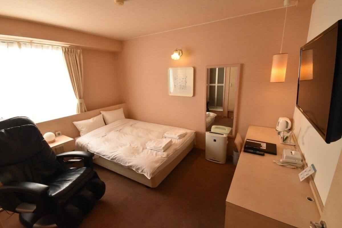 A hotel room with a bed, a massage chair, a desk with a computer, a telephone, and a mirror.