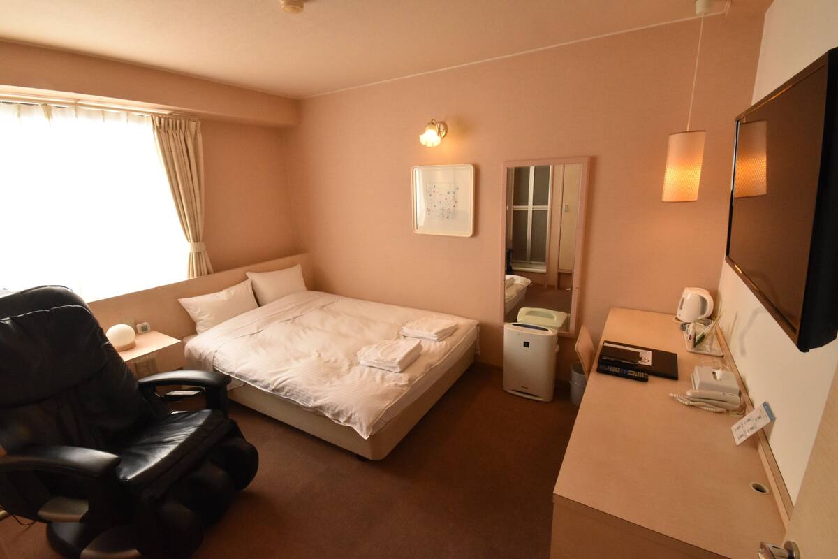 A hotel room with a bed, a massage chair, a desk with a computer, a telephone, and a mirror.