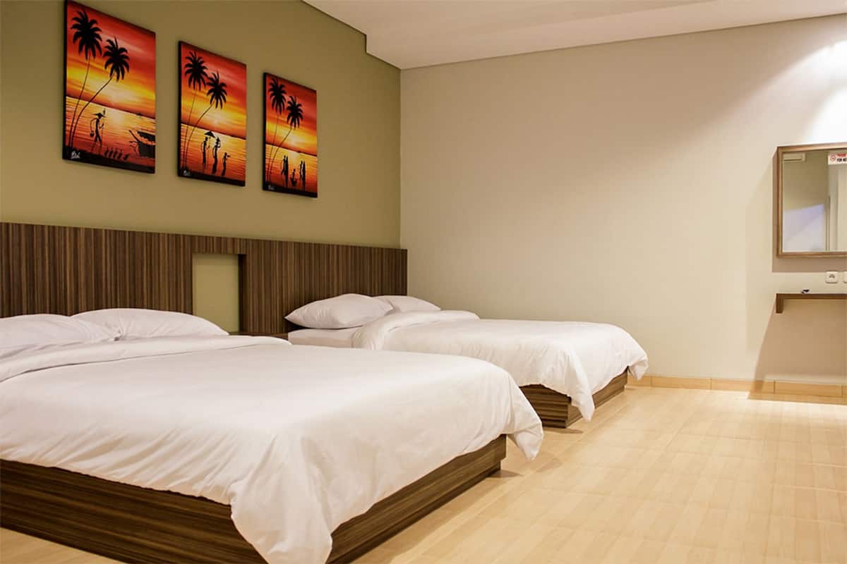 A hotel room with three single beds, a wooden headboard, a large mirror, and three sunset-themed paintings on the wall.