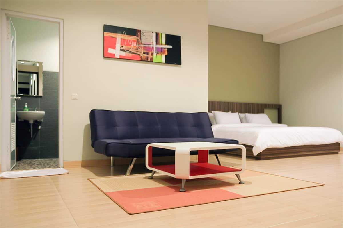 A modern bedroom with a bed, a blue sofa, a small table, and a painting on the wall.