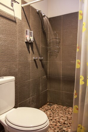 A bathroom with a toilet, a shower, and a tiled floor. - Link Costel (Denpasar)